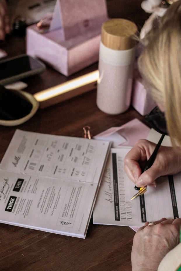 A workshop attendee with blonde hair holding a calligraphy pen and writing on a worksheet in a Calligraphy Workshop in Sydney