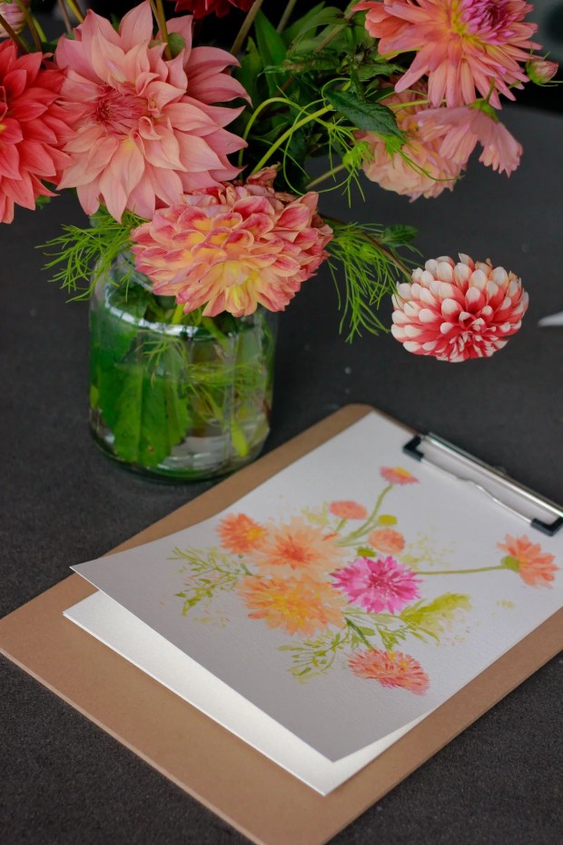 A jar of freshly-harvest dahlias in orange and pink tones with a recently finished watercolour artwork in a loose painting style as learned from the Watercolour Loose Florals Workshop run by Gizelle 